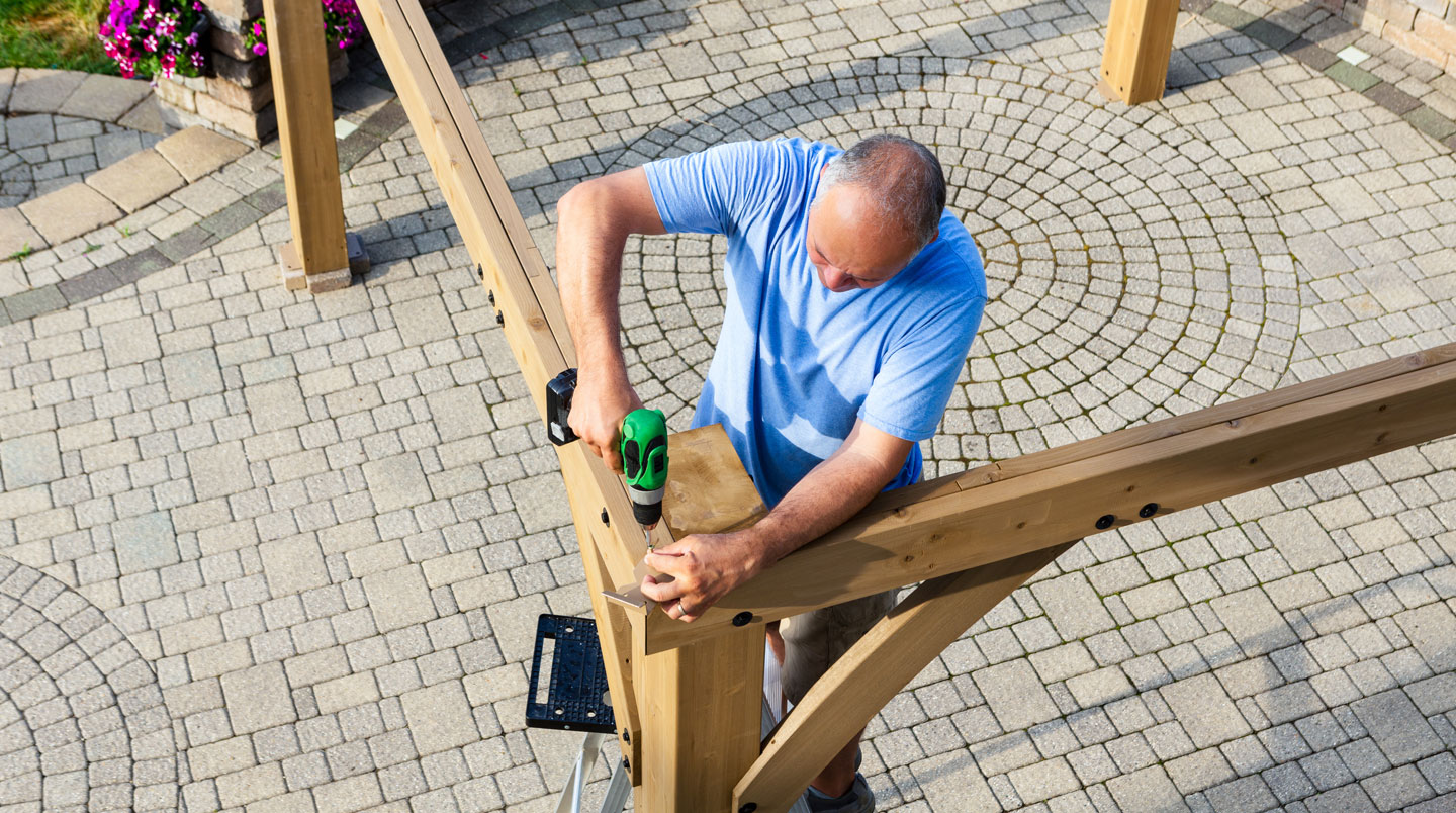 Instalador profesional ensamblando perfiles de aluminio de un carport, visto desde atrás, enfoque en las manos trabajando con la estructura metálica en un jardín residencial