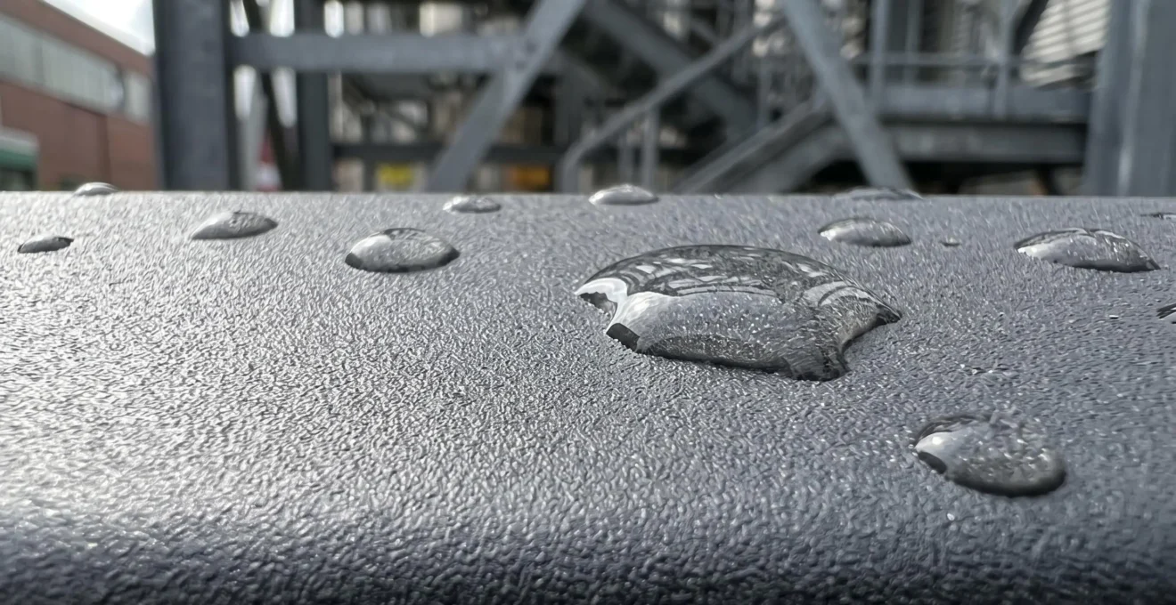 Primer plano extremo de la superficie de aluminio termolacado con gotas de agua deslizándose sobre el revestimiento protector